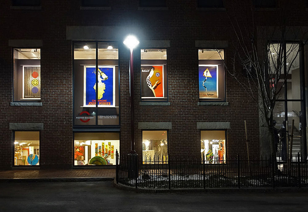 Night view into the gallery with posters lit up in windows