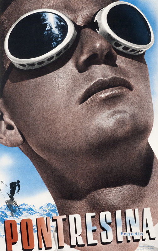 Close up view of man with ski goggles on, view of mountain and skiier behind; blue, black red, white