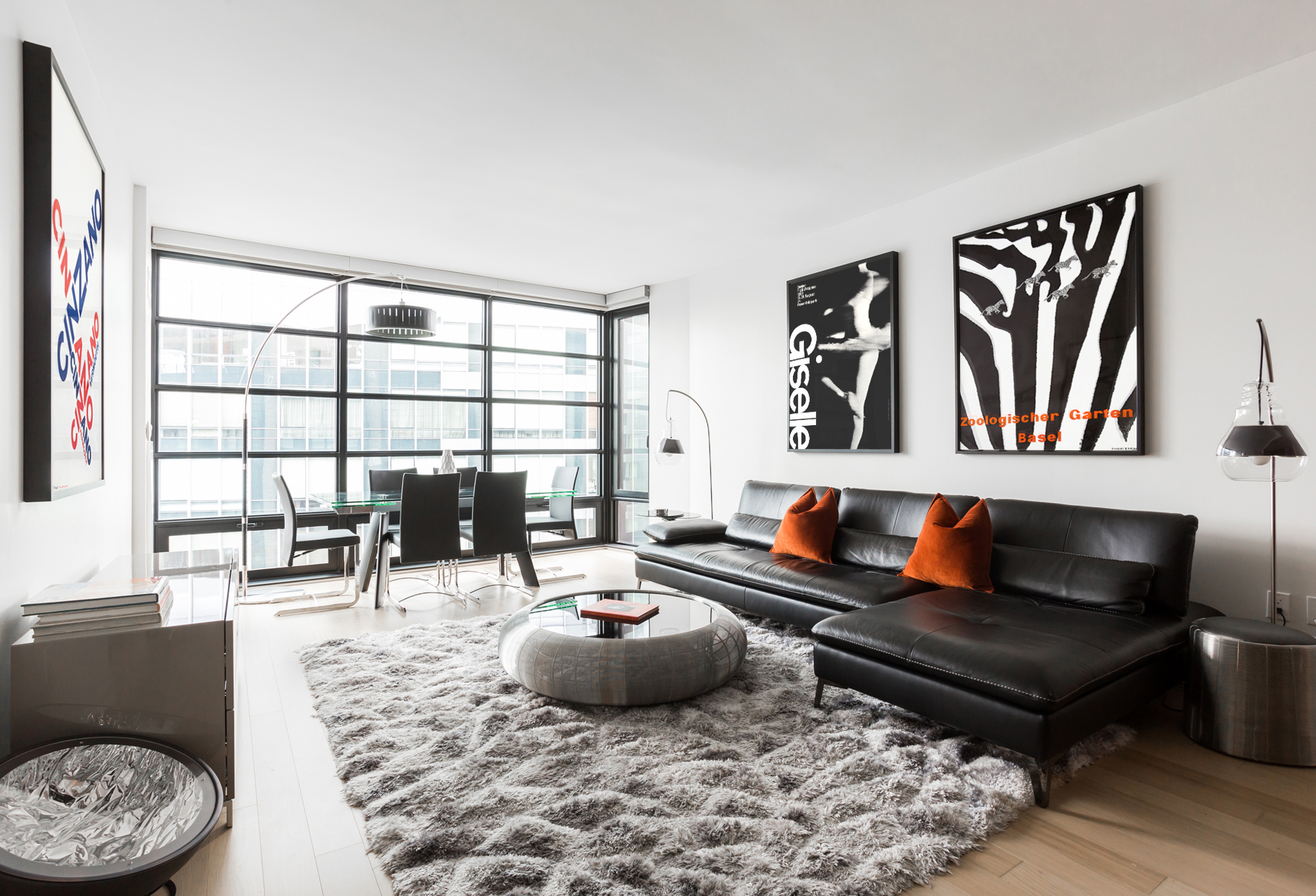 Minimalist living room with window wall, fuzzy rug, and posters above couch; red, black, grey